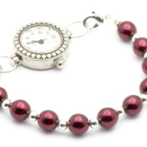 May include: A silver watch with a white face and black hands attached to a bracelet of maroon beads.