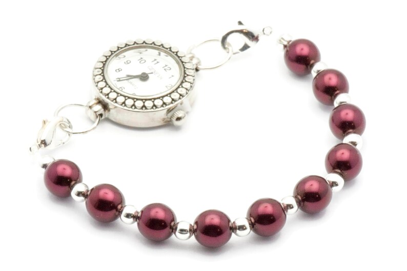 May include: A silver watch with a white face and black hands attached to a bracelet of maroon beads.