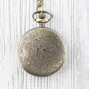 Pode incluir: Um rel&oacute;gio de bolso dourado com um design floral decorativo no mostrador. O rel&oacute;gio est&aacute; pendurado em uma corrente.