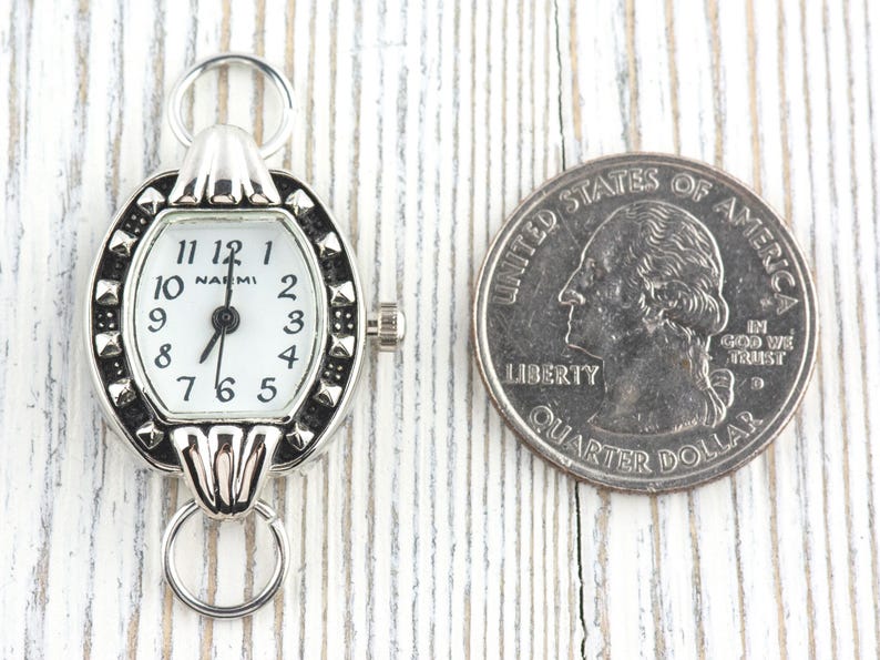 May include: A silver pocket watch with a white face and black numerals, next to a quarter. The watch has a decorative bezel and a ring for attachment. The quarter is a United States quarter dollar.