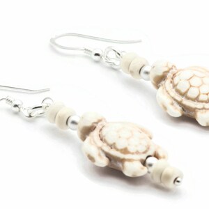 May include: A pair of silver dangle earrings with white turtle charms and white beads.