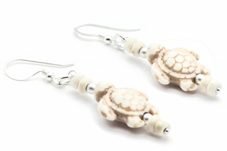 May include: A pair of silver dangle earrings with white turtle charms and white beads.