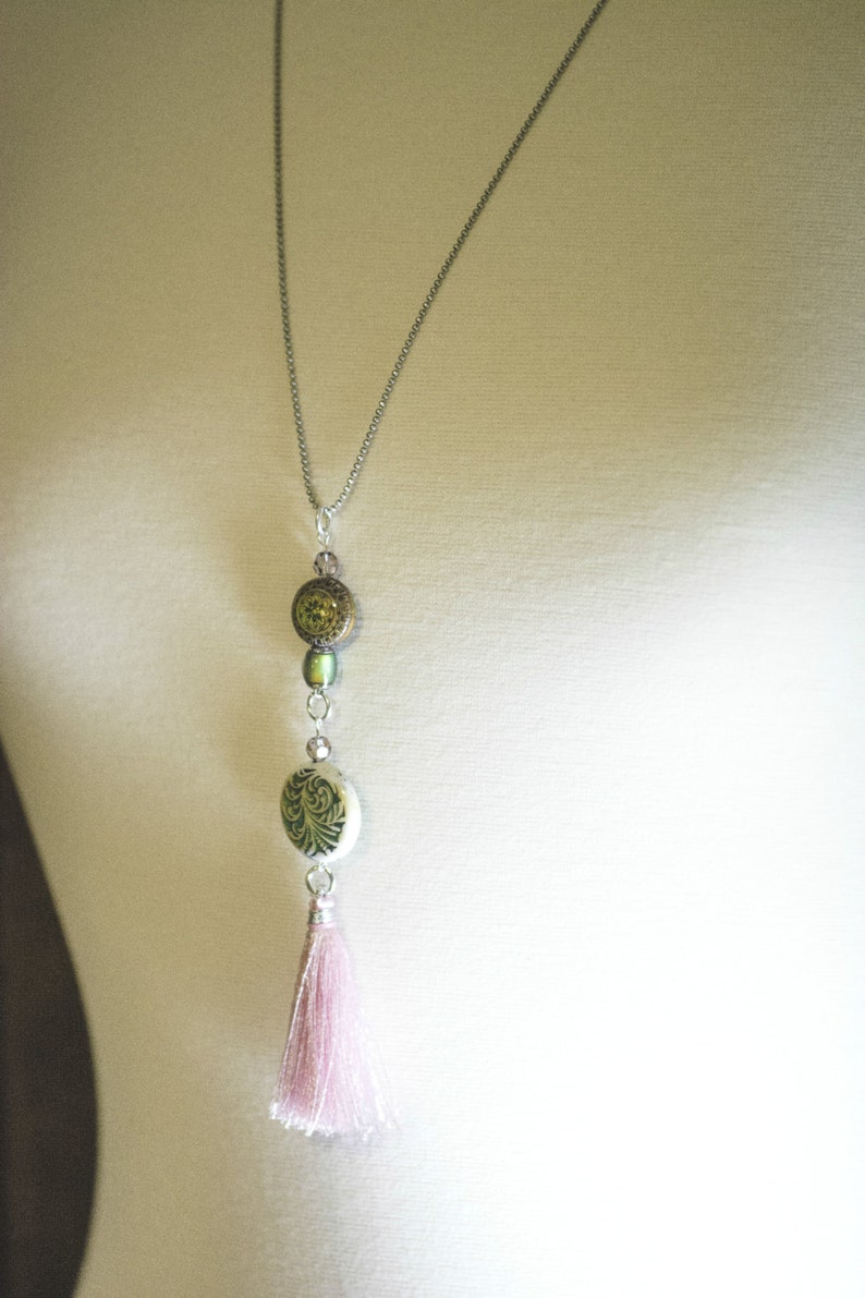May include: A silver chain necklace with a pink tassel, a green and white patterned bead, and a green and gold bead.