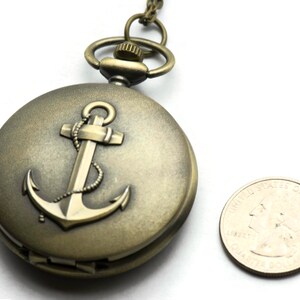 May include: A bronze pocket watch with an anchor design on the face. The watch is about the size of a US quarter.