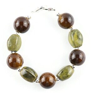 May include: A brown and green ceramic bead bracelet with a silver clasp. The bracelet has round and oval beads.