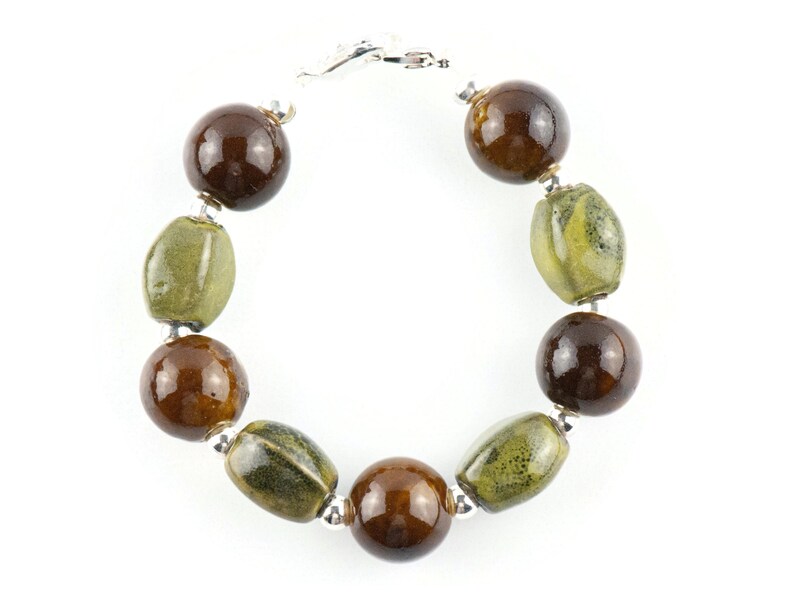 May include: A brown and green ceramic bead bracelet with a silver clasp. The bracelet has round and oval beads.