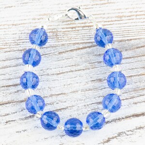 Pu&ograve; includere: Un braccialetto con perline di cristallo blu con una chiusura argentata. Le perline sono sfaccettate e hanno un colore blu chiaro.