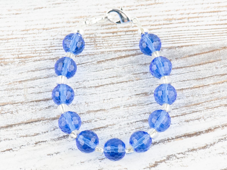Pu&ograve; includere: Un braccialetto con perline di cristallo blu con una chiusura argentata. Le perline sono sfaccettate e hanno un colore blu chiaro.