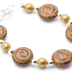 May include: A bracelet with large, round, brown and green glass beads, each with a spiral pattern. It also features smaller olive-green beads and silver-coloured spacer beads. A silver-coloured clasp secures the bracelet.