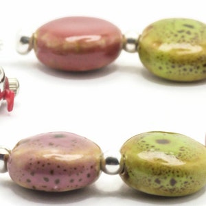 May include: A silver watch with a white face and black hands is attached to a bracelet made of colourful ceramic beads. The beads are in shades of green, pink, and grey.