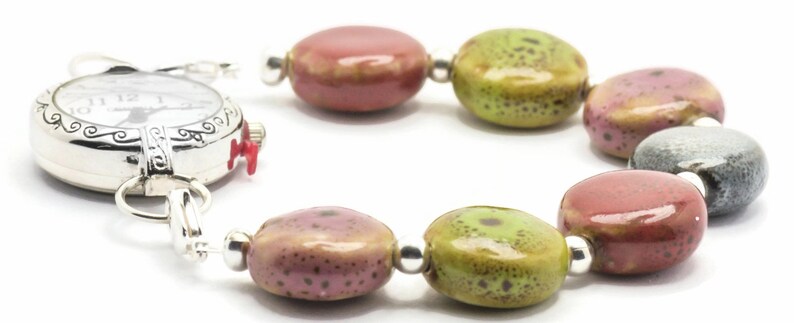 May include: A silver watch with a white face and black hands is attached to a bracelet made of colourful ceramic beads. The beads are in shades of green, pink, and grey.