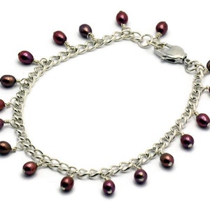 May include: A silver chain bracelet with a lobster clasp and multiple dangling dark purple pearls.