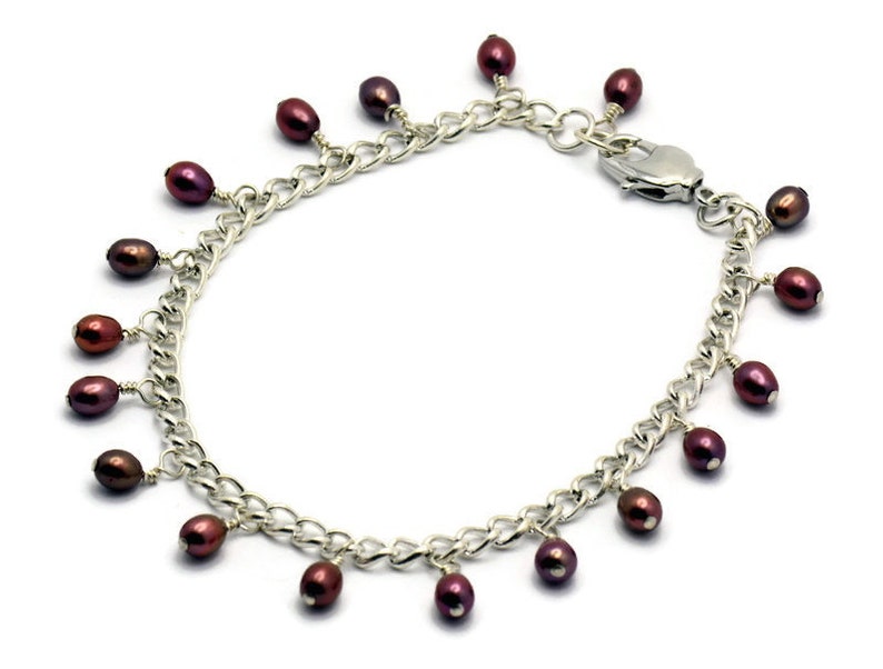 May include: A silver chain bracelet with a lobster clasp and multiple dangling dark purple pearls.
