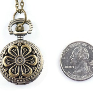 May include: A bronze-colored pocket watch with a floral design on the face. The watch is attached to a chain and is about the size of a quarter.