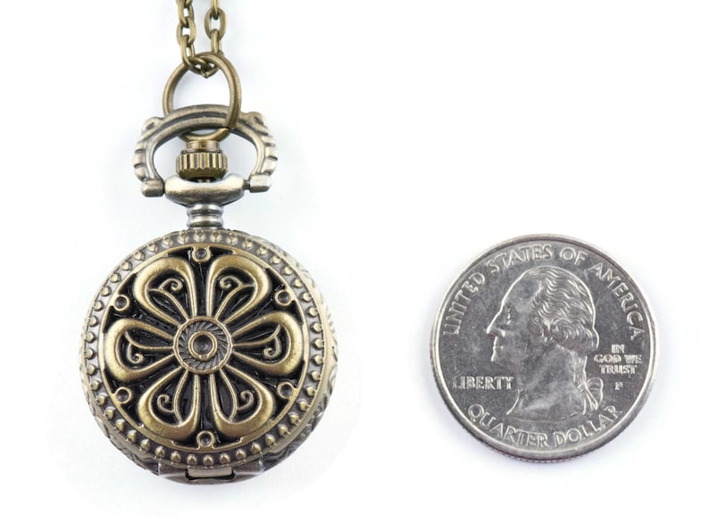 May include: A bronze-colored pocket watch with a floral design on the face. The watch is attached to a chain and is about the size of a quarter.