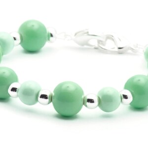 May include: A green and silver beaded bracelet with a silver clasp. The beads are round and have a gradient of green.