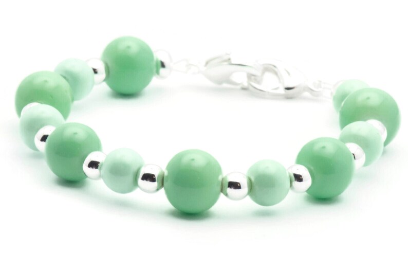 May include: A green and silver beaded bracelet with a silver clasp. The beads are round and have a gradient of green.