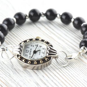 Peut inclure: Une montre Geneva &agrave; quartz avec un bo&icirc;tier argent&eacute; et un cadran blanc, avec des chiffres et des aiguilles noirs. La montre est attach&eacute;e &agrave; un bracelet compos&eacute; de perles noires et rondes. La montre a un fermoir argent&eacute;.