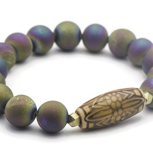 May include: A bracelet made of iridescent agate beads with a brown wooden bead with a carved design in the center.