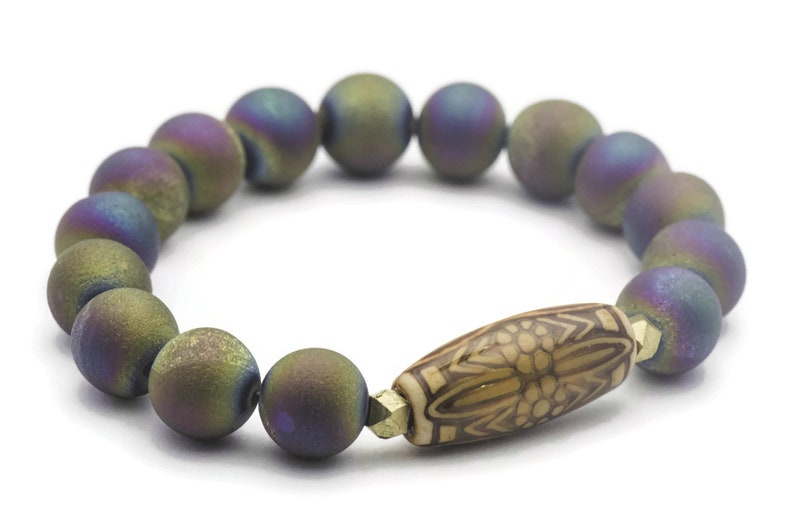 May include: A bracelet made of iridescent agate beads with a brown wooden bead with a carved design in the center.