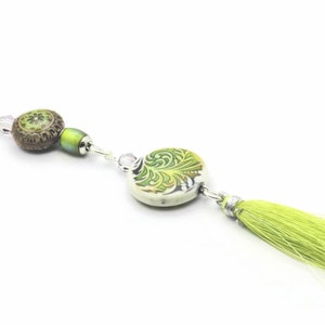May include: A green and brown beaded necklace with a green tassel. The necklace features a round ceramic pendant with a green and white floral design.