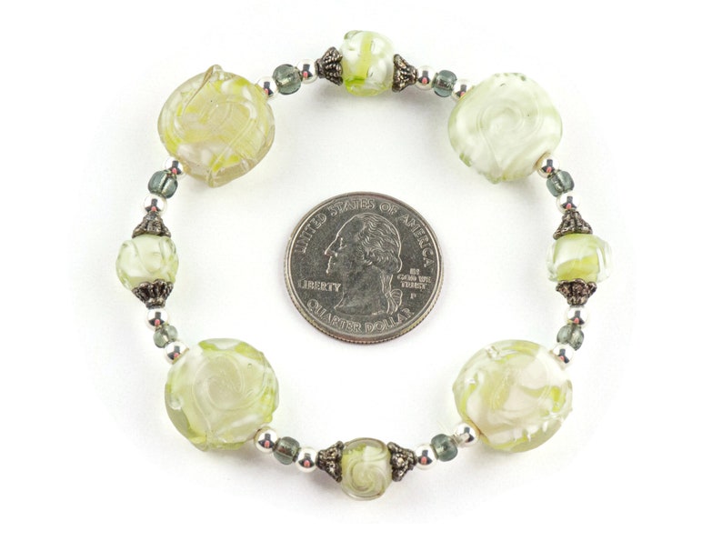 Peut inclure: Un bracelet en verre vert avec des motifs de fleurs grav&eacute;s et des accents argent&eacute;s. Le bracelet est &agrave; peu pr&egrave;s de la taille d'une pi&egrave;ce de 25 centimes.