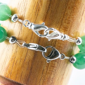 May include: Two green gemstone bracelets with silver clasps and silver beads. The bracelets are displayed on a wooden surface.