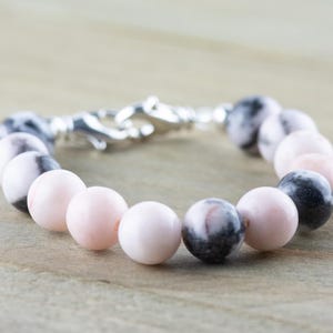 May include: A bracelet made with pink and black marbled beads and a silver clasp.