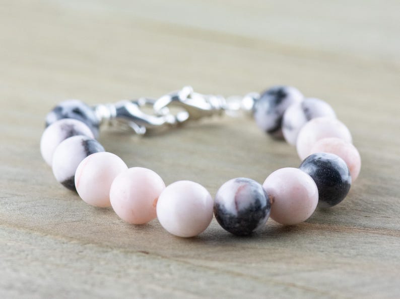 May include: A bracelet made with pink and black marbled beads and a silver clasp.