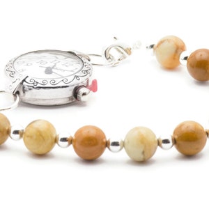 May include: A silver watch with a white face and black Roman numeral markings is attached to a bracelet made of brown and beige stones.