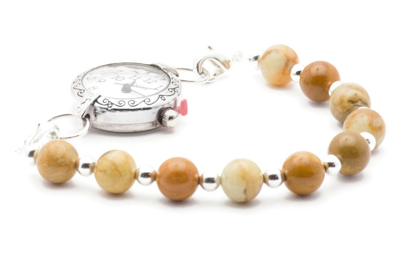 May include: A silver watch with a white face and black Roman numeral markings is attached to a bracelet made of brown and beige stones.
