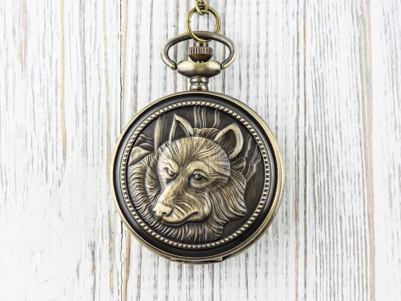 May include: A gold-toned pocket watch with a wolf head design on the face. The watch has a chain attached to it.