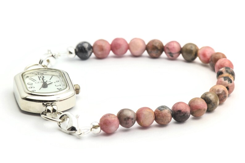 K&ouml;nnte beinhalten: Eine silberne Uhr mit quadratischem Zifferblatt und einem Armband aus rosa und braunen Perlen.