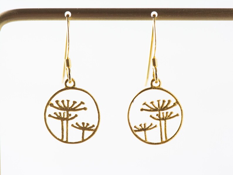 May include: Gold dangle earrings with a circular design featuring three stylized flower silhouettes.