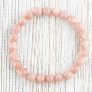 May include: A pink sunstone bracelet with round beads on a white wooden background.