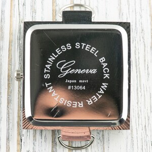 May include: The back of a silver square watch with a black face. The watch has the words "Stainless Steel Back Water Resistant" and "Geneva Japan movt #13064" engraved on the back.