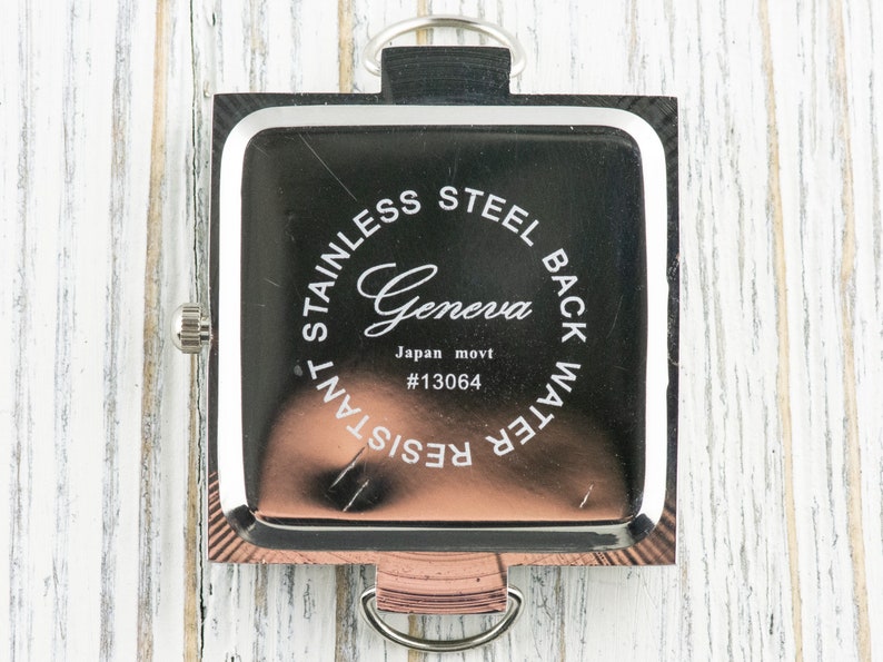 May include: The back of a silver square watch with a black face. The watch has the words "Stainless Steel Back Water Resistant" and "Geneva Japan movt #13064" engraved on the back.