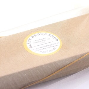 K&ouml;nnte beinhalten: Ein in hellbraunes Papier verpacktes Paket, mit Bindfaden verschn&uuml;rt und in einem durchsichtigen, wei&szlig;en Stoff eingeschlossen. Ein gelber Aufkleber mit schwarzem Text lautet "Black Brook Shop" und "handmade."