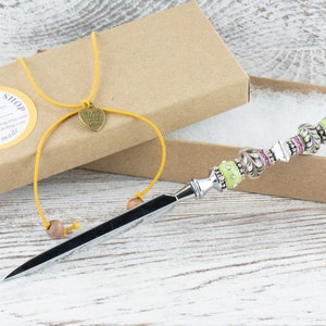 Peut inclure: Un ouvre-lettre en argent avec un manche en perles vertes et roses. Le manche est d&eacute;cor&eacute; de strass et de volutes. L'ouvre-lettre est dans une bo&icirc;te brune avec une ficelle jaune et un charme en forme de c&oelig;ur qui dit "Fait &agrave; la main avec amour".