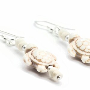 May include: A pair of silver dangle earrings with white turtle charms and white beads.