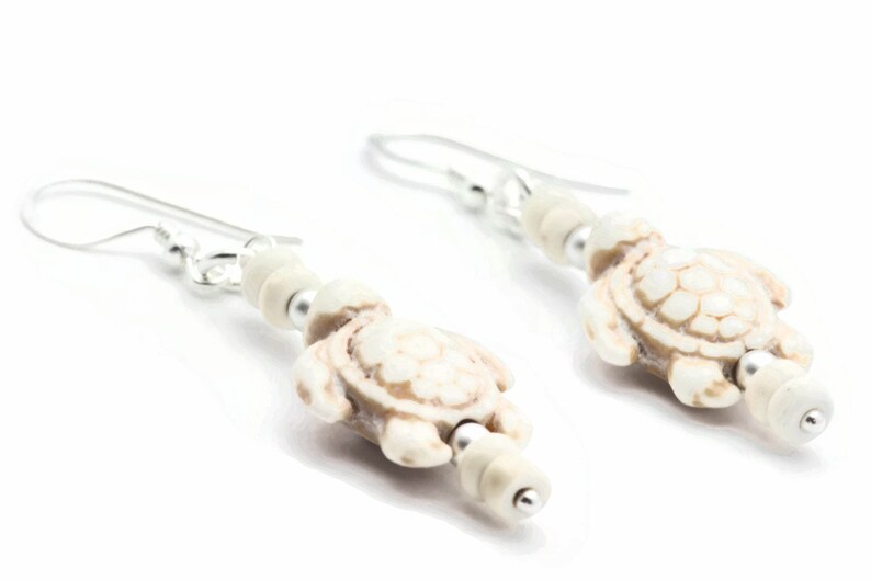 May include: A pair of silver dangle earrings with white turtle charms and white beads.