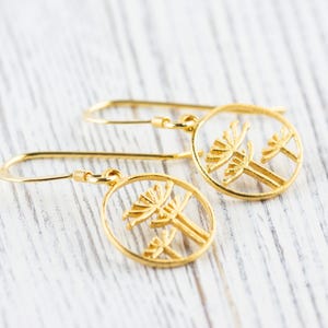 May include: A pair of gold dangle earrings with a delicate design of two stylized trees in a circle.