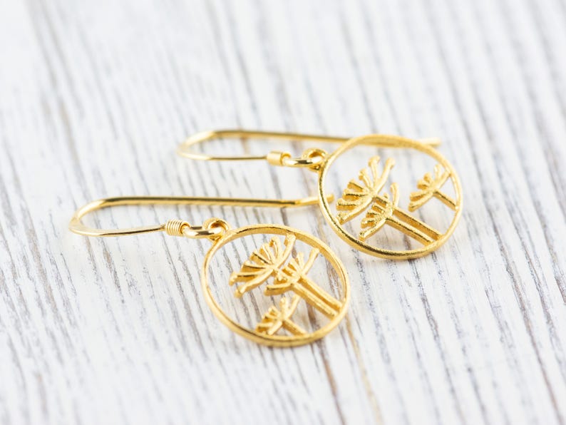 May include: A pair of gold dangle earrings with a delicate design of two stylized trees in a circle.