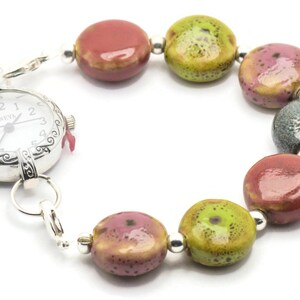 May include: A silver watch with a white face and black hands attached to a bracelet made of colourful ceramic beads. The beads are red, green, and grey.