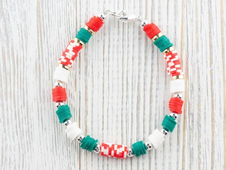 May include: A green, red, and white beaded bracelet with a silver clasp. The beads are stacked in a repeating pattern.