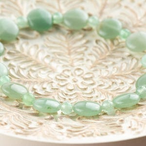 Peut inclure: Un bracelet en pierres pr&eacute;cieuses vertes avec des perles de forme ovale. Le bracelet est sur un fond blanc avec un motif floral.