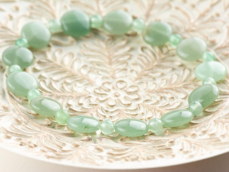 Peut inclure: Un bracelet en pierres pr&eacute;cieuses vertes avec des perles de forme ovale. Le bracelet est sur un fond blanc avec un motif floral.