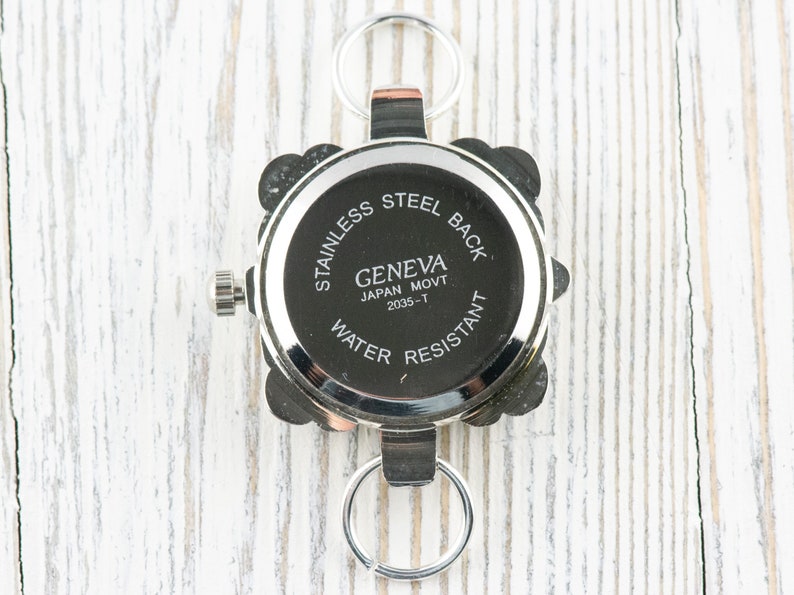 May include: Silver watch with a square face and a stainless steel back. The watch has a Geneva Japan Movt 2035-T movement and is water resistant.