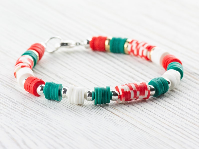 May include: A red, white, and green beaded bracelet with silver accents. The bracelet is made of round and cylindrical beads.