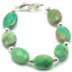 May include: A green gemstone bracelet with silver beads and a silver clasp. The bracelet is made of oval-shaped green stones with a mottled pattern.